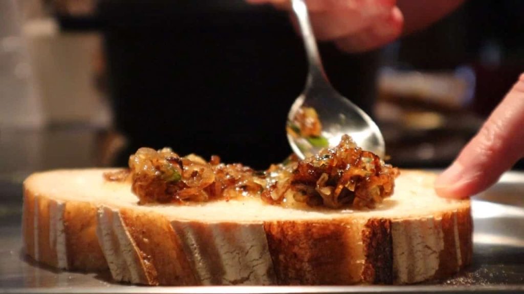 Caramelized onions being spread on a slice of bread with a spoon