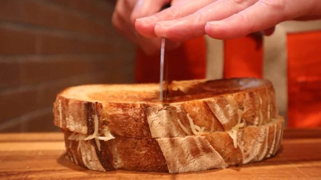 Close up of knife cutting a grilled cheese sandwich