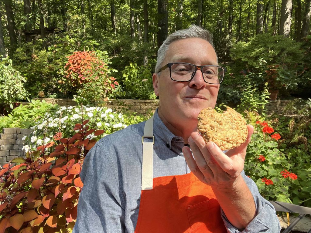 Tim taking a big bite out of an oatmeal raisin chocolate chip cookie.