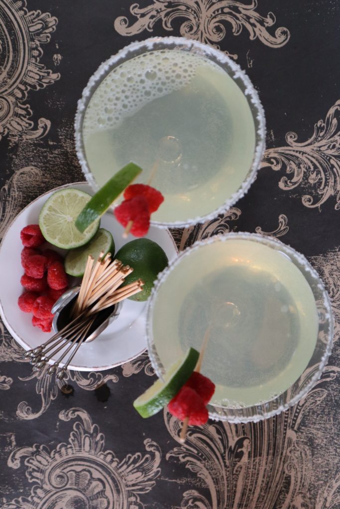 Raspberry margarita cocktails in glasses with lime and raspberry garnishes.
