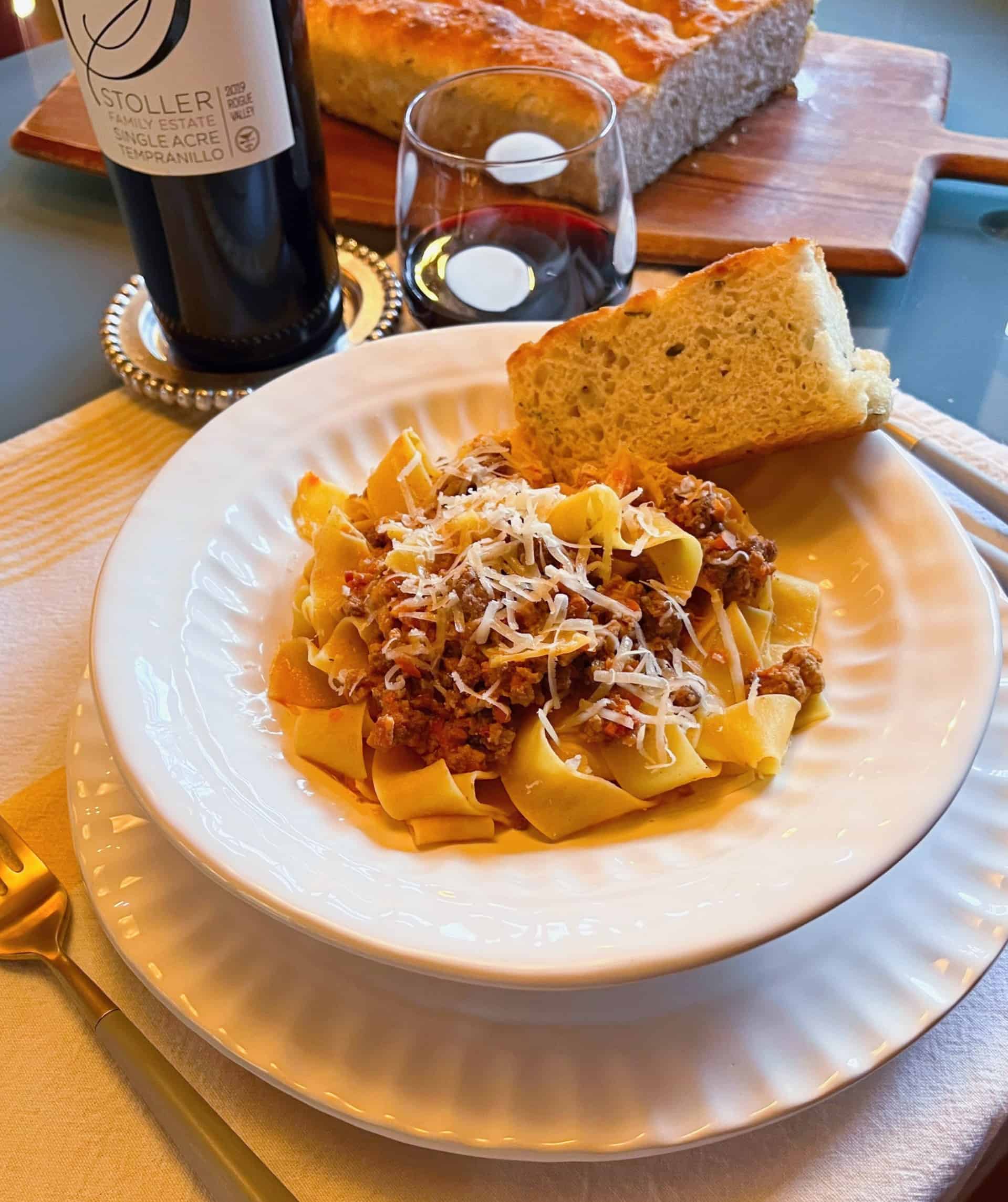 Lamb bolognese in pasta bowl with focaccia and wine