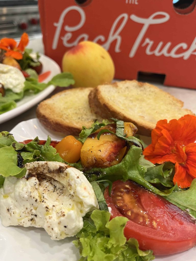 Close up of plate with peach slices, burrata, greens, and a crusty bread
