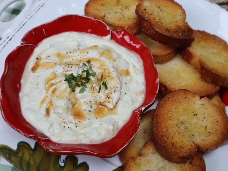 Red bowl filled with whipped ricotta on a platter with crostini