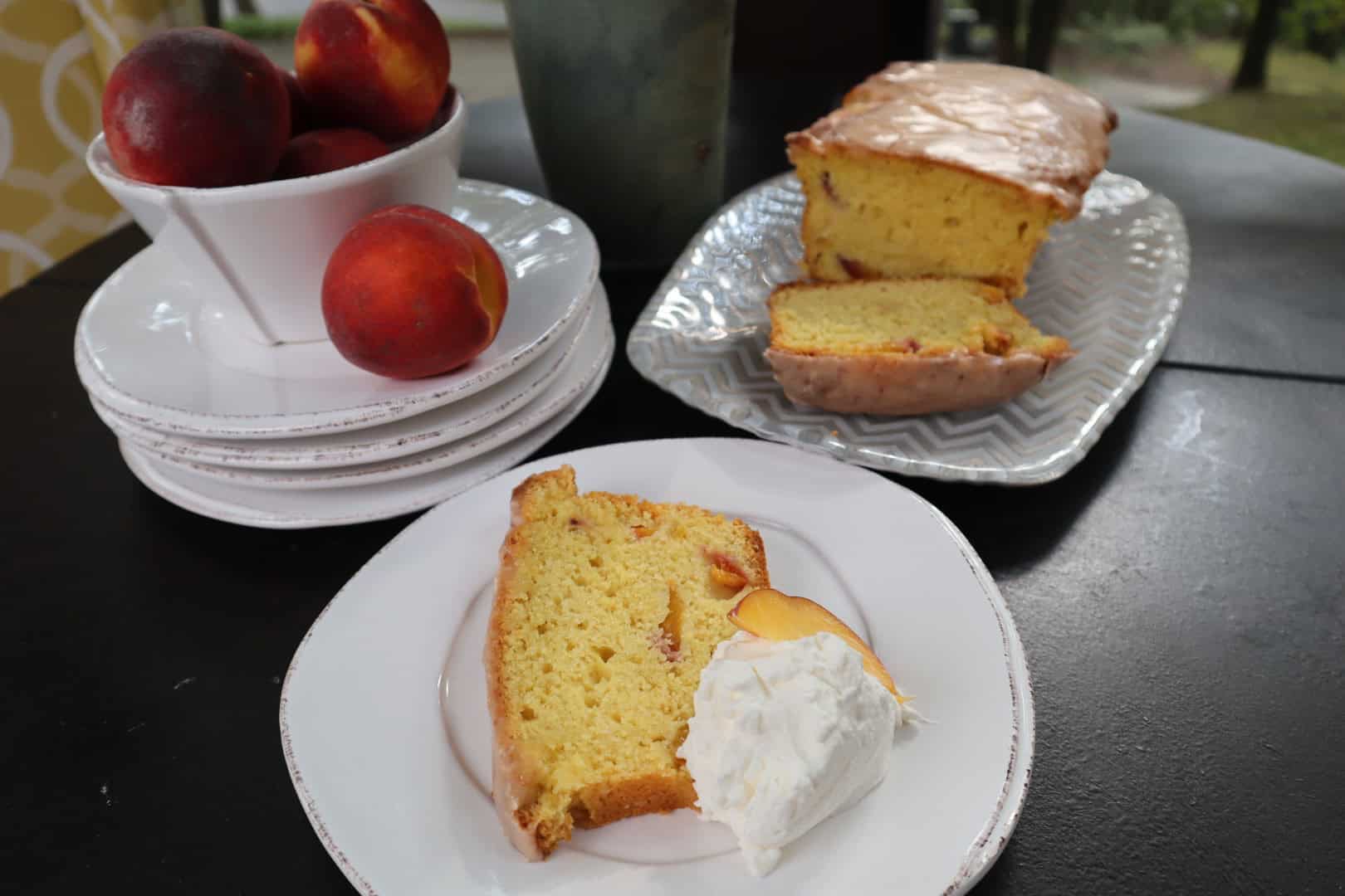 A slice of peach pound cake on a plate with sweet cream and the entire cake in the background.