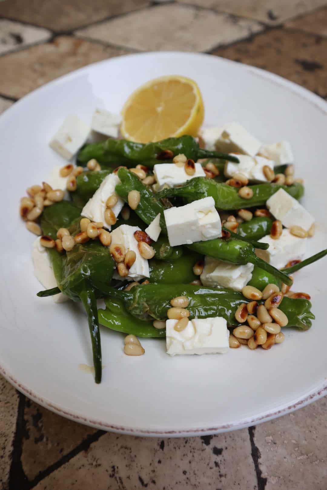 Bowl filled with Blistered Shishito Pepper Salad, with feta and pine nuts.