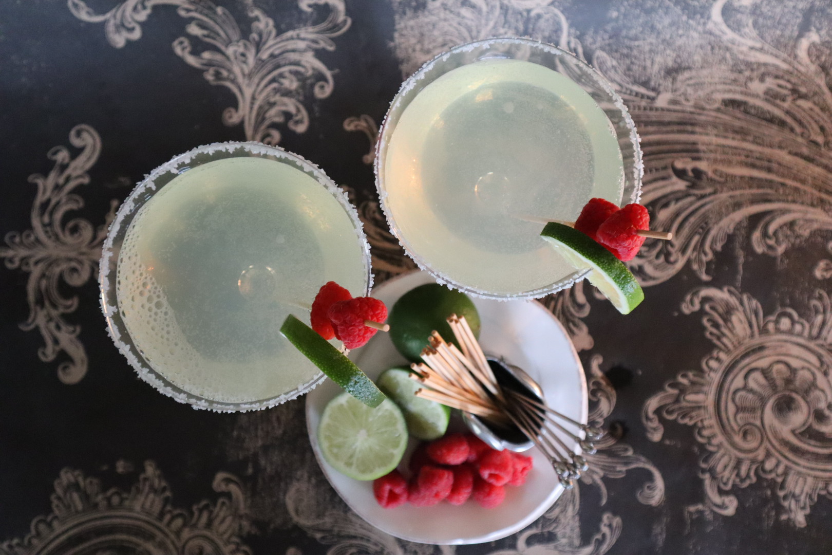 Raspberry margarita cocktails in glasses with lime and raspberry garnishes.
