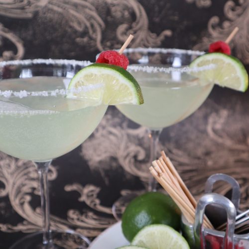 Raspberry margarita cocktails in glasses with lime and raspberry garnishes.